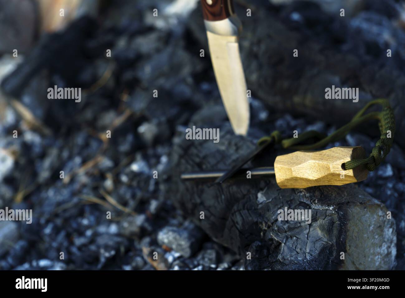 Überlebensmesser und Ferro-Stab liegen auf verbranntem Holz und Holzkohle und repräsentieren Outdoor-Abenteuer und Bushcraft-Fähigkeiten Stockfoto