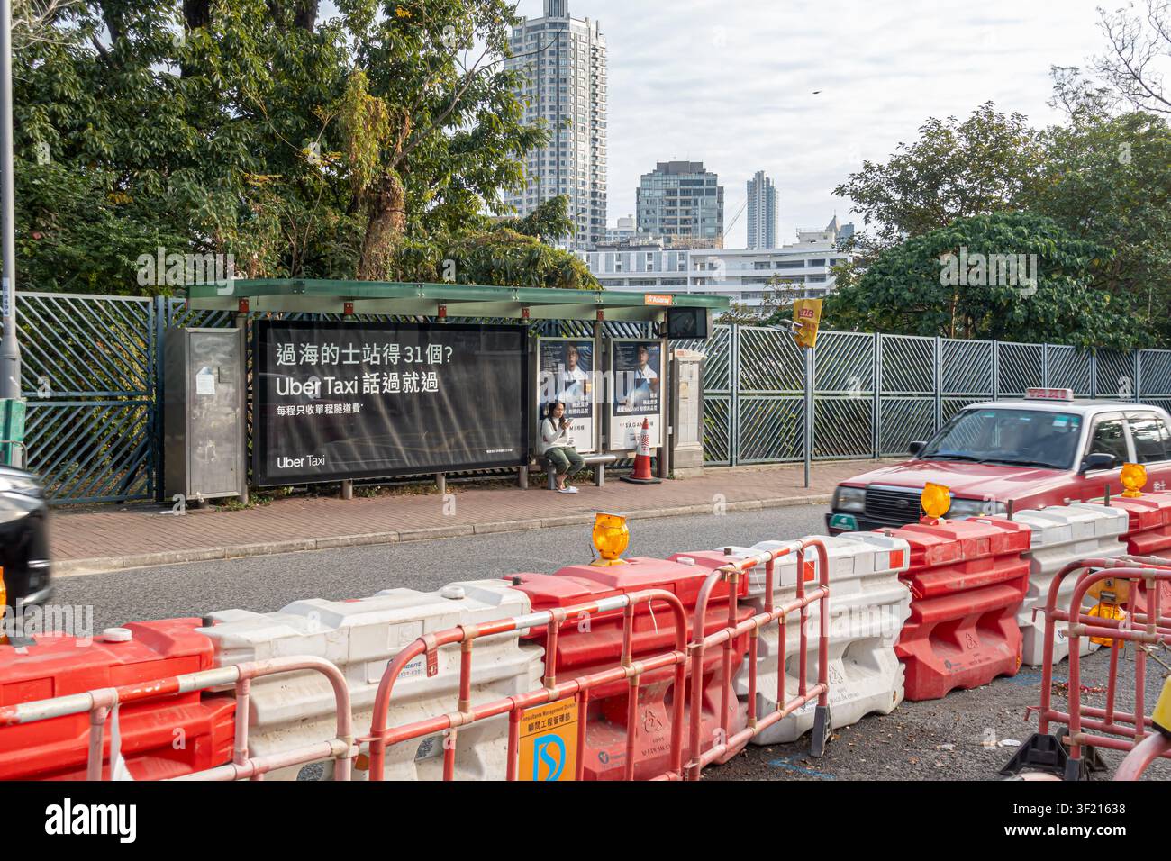 öffentliche Bushaltestelle und Straßenrand, Mong Kok, Hongkong, mit einer großen Werbung für einen Taxidienst, Plastiksicherungsbarrieren, die Straßenbauarbeiten anzeigen Stockfoto