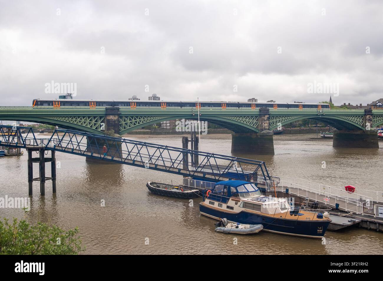 LONDON – 19. MAI 2026: Wandsworth Bridge – Grüne Stahlbrücke mit Zug der District Line und festgemachten Booten auf der Themse bei Ebbe. Stockfoto