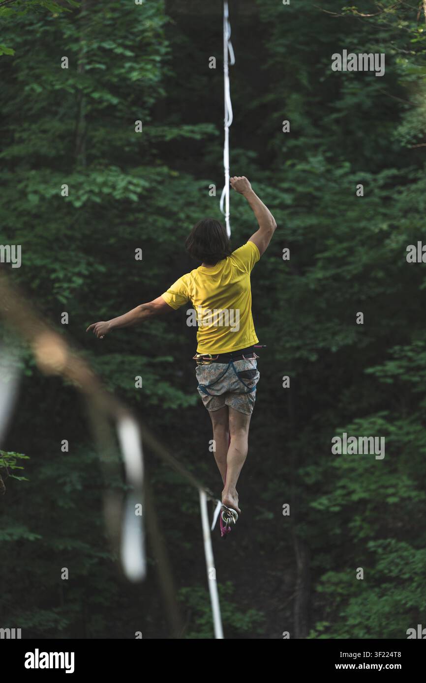 Highline-Wanderer Slackline-Balancieren Wald Extremsport Abenteuer Risiko Herausforderung Motivation Fokus gelbes Hemd Stockfoto