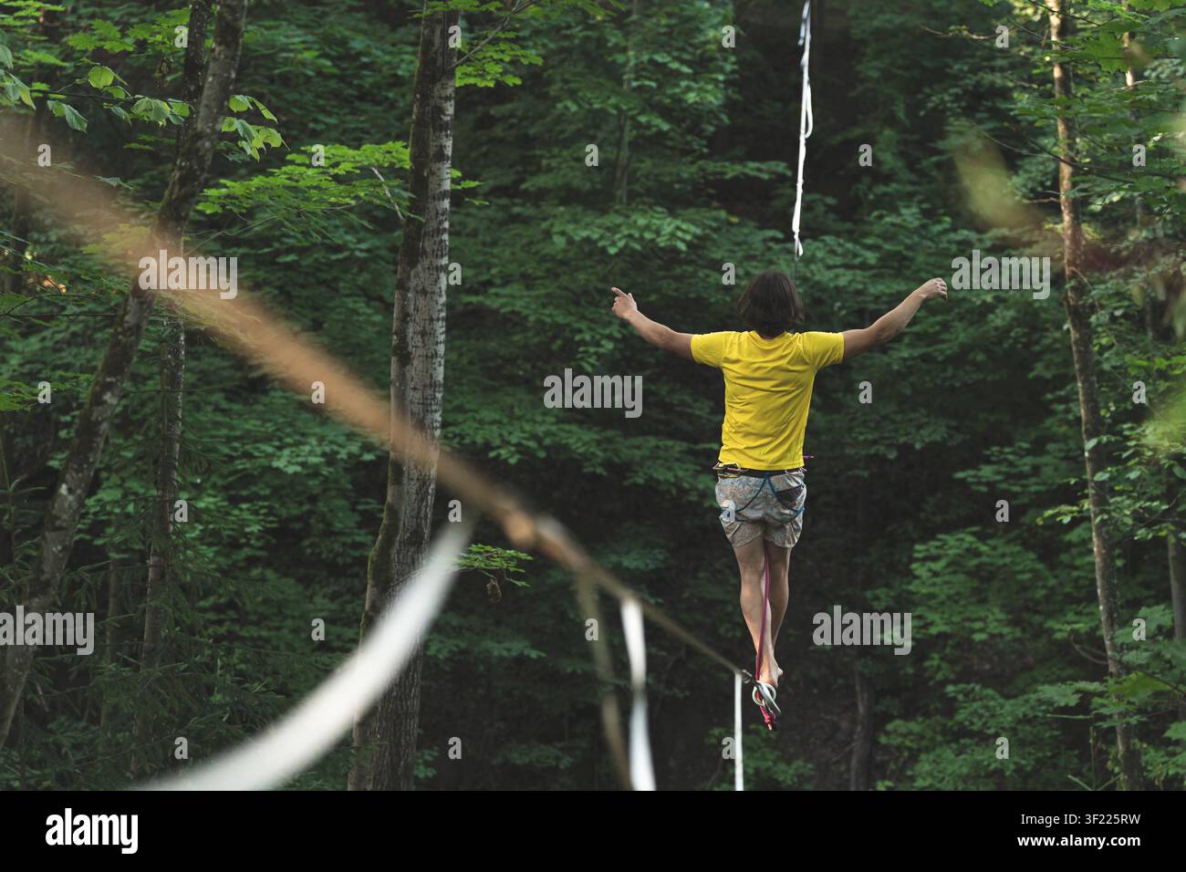 Highline-Wanderer Slackline-Balancieren Wald Extremsport Abenteuer Risiko Herausforderung Motivation Fokus gelbes Hemd Stockfoto