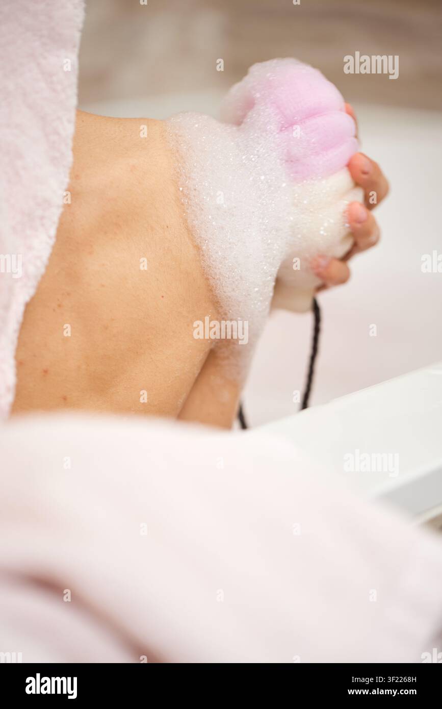 Person, die eine Dusche nimmt und ihren Körper mit einem Schwamm wäscht Stockfoto