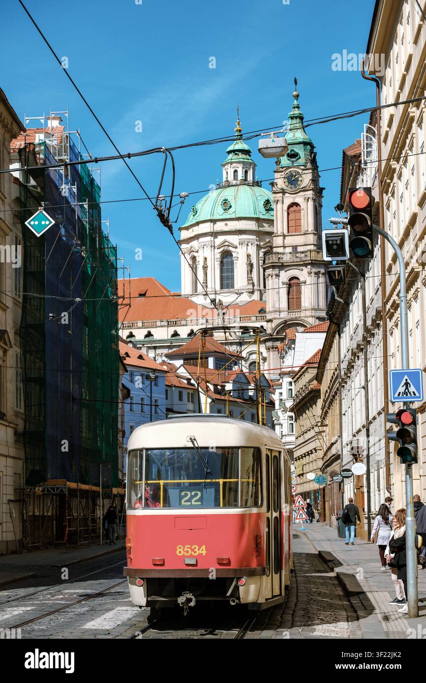 Prag, Tschechien, 8. April 2026, fährt Eine lebhafte Straßenbahn entlang der kopfsteingepflasterten Straßen von Prag, eingerahmt von atemberaubender barocker Architektur. Stockfoto