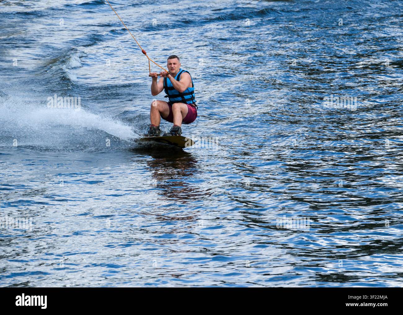 Kiew, Ukraine - 11. Juli 2026: Ein Wakeboard-Fahrer fährt in tiefer Kniebeuge, während er das Board beladet und sich auf den Sprung vorbereitet während eines Stockfoto
