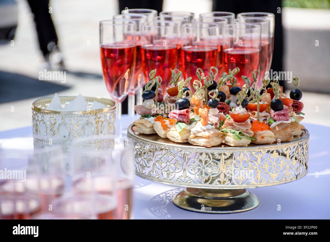 Elegante Außencatering-Ausstattung auf einer weißen Tischdecke, mit vorgefüllten Getränken und kleinen Häppchen, bereit für eine Feier Stockfoto