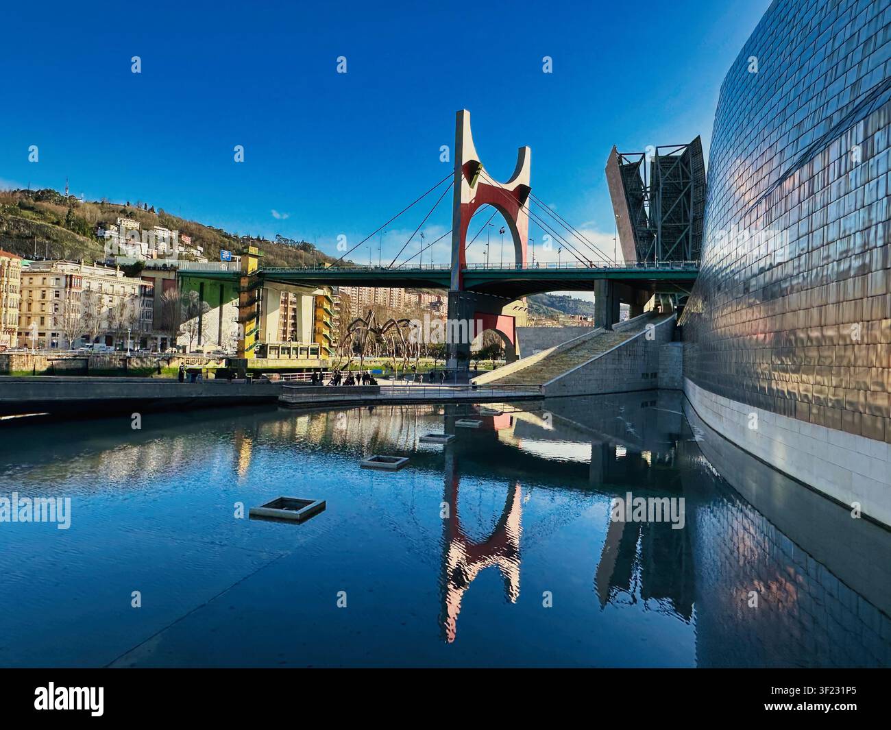 Bilbao, Spanien - 23. Dezember 2025: Blick auf das Guggenheim Museum Bilbao mit seinen Titankurven, die sich im Wasser spiegeln, mit der Brücke La Salve im Vordergrund Stockfoto