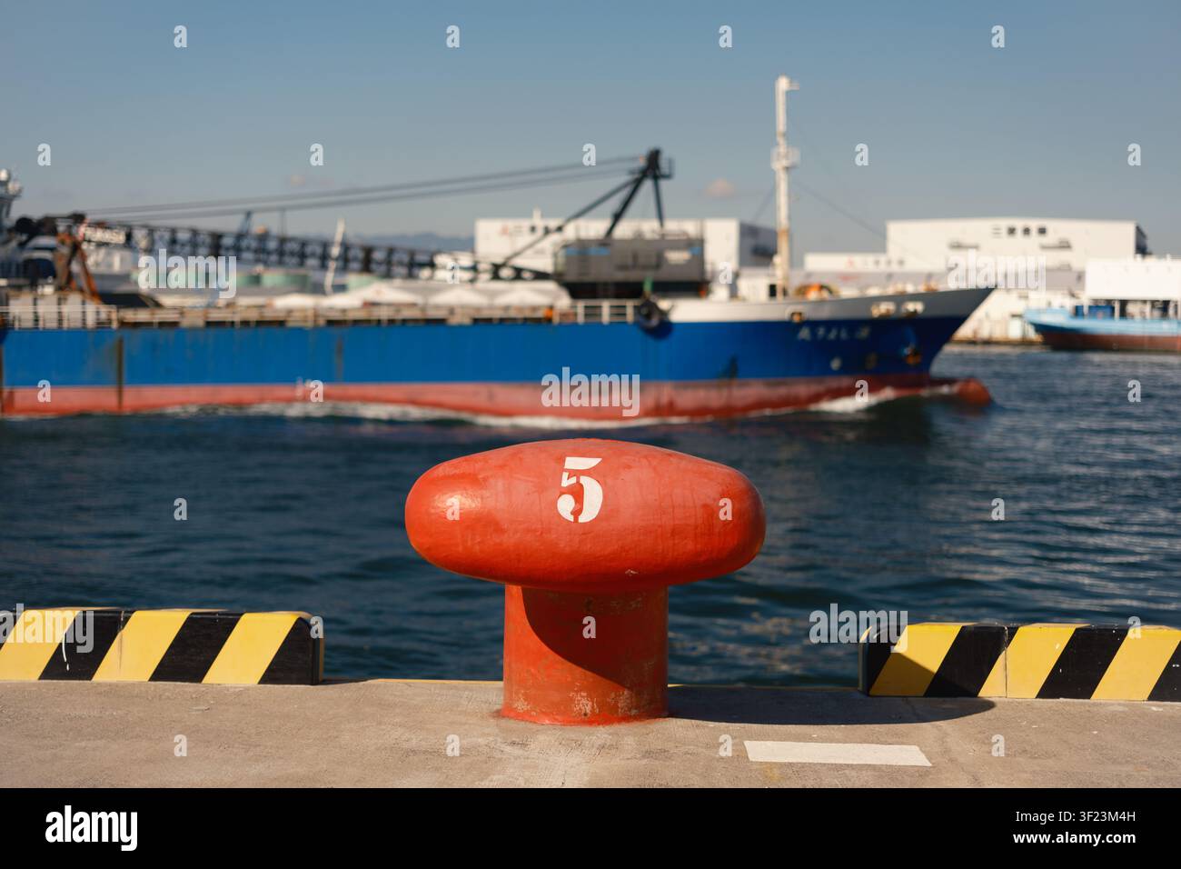 Ein roter Ankerbollwerk aus Gusseisen, der auf einem Hafensteg steht, mit einem kommerziellen Frachtschiff im Hintergrund, Osaka, Japan. Stockfoto