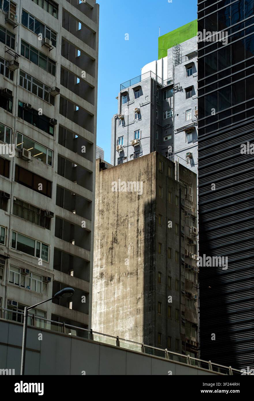 Bild von kontrastierenden Stadthochhäusern, das ein verwittertes Betongebäude zeigt, das zwischen modernen Handelstürmen unter blauem Himmel eingeklemmt ist Stockfoto