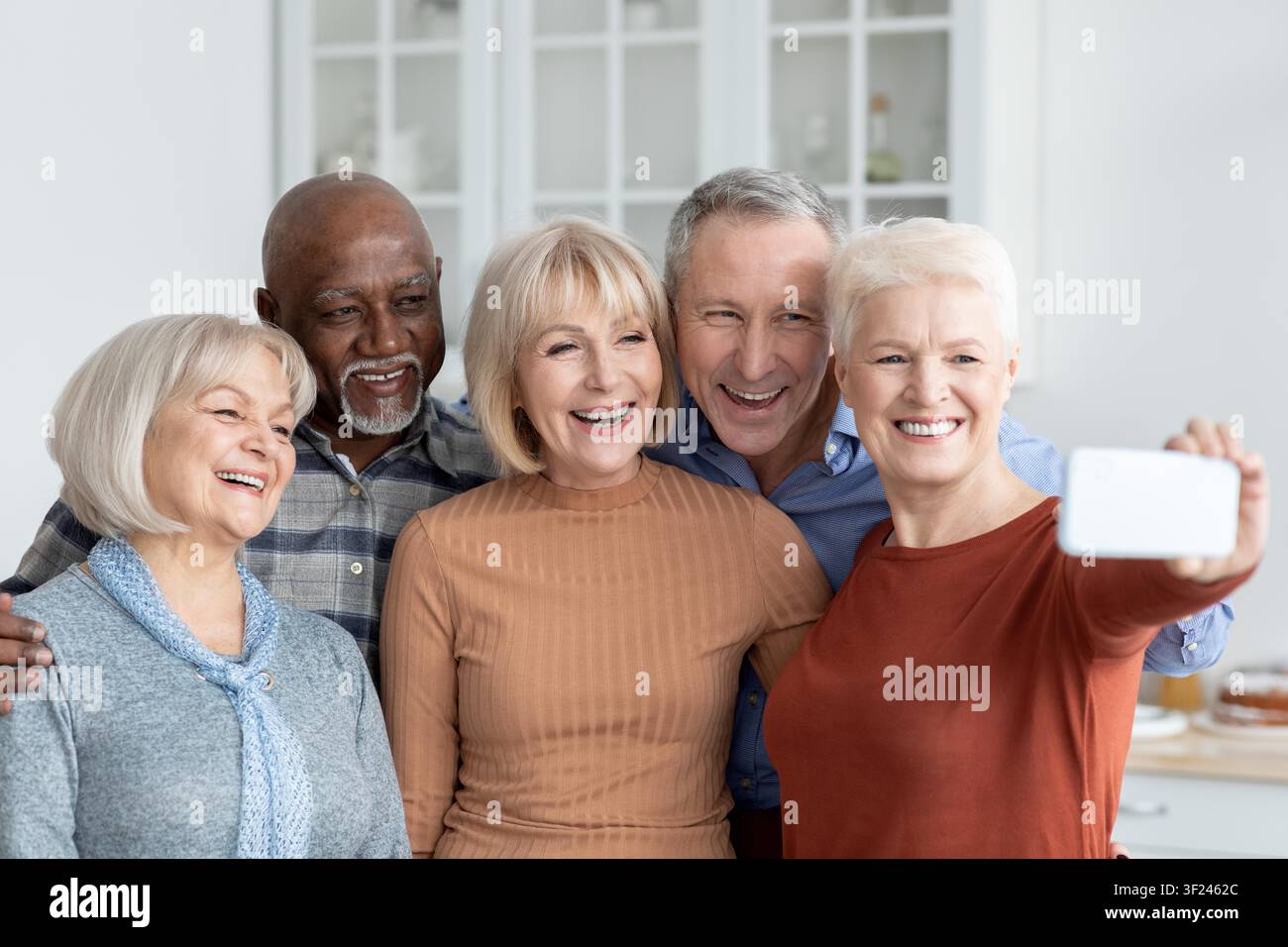 Fünf glückliche Senioren lächeln zusammen und machen ein Selfie in der Küche, ein freudiger Moment Stockfoto