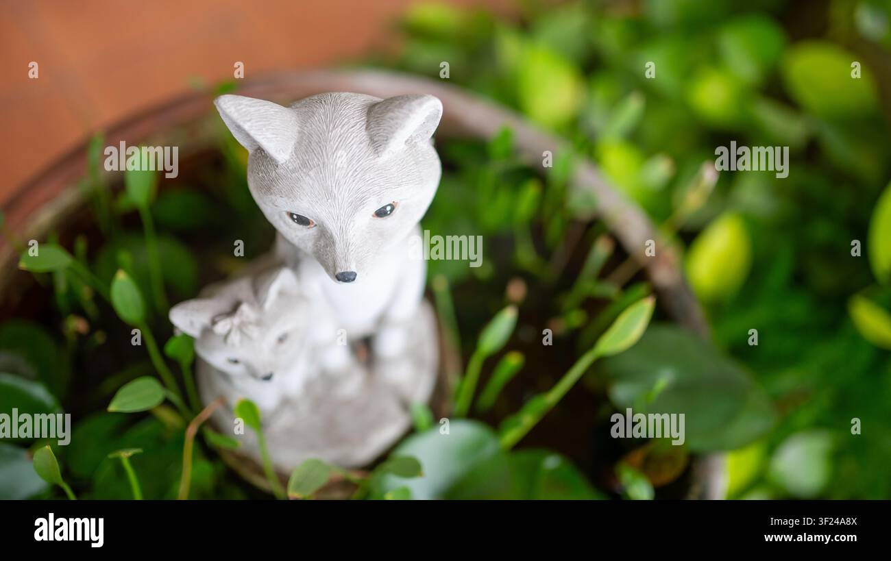 Diese realistische Fuchsskulptur ist von üppigen grünen Pflanzen umgeben und fügt Gärten im Freien oder der Heimdekoration ein charmantes und von der Natur inspiriertes Element hinzu Stockfoto