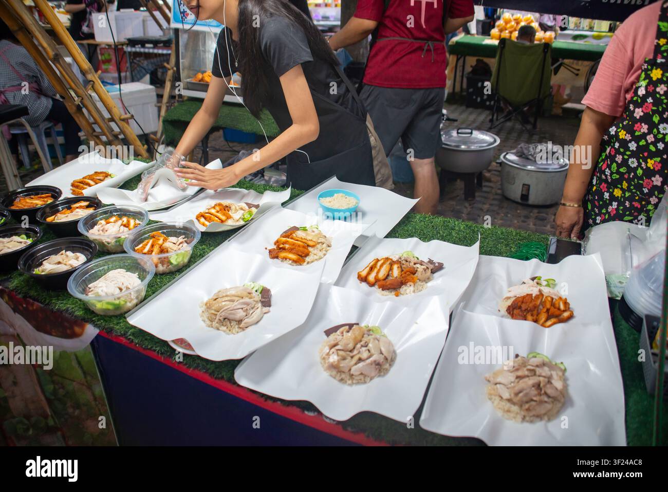 Eine geschäftige Nachtmarkt-Szene mit einem Stand, auf dem eine Vielzahl traditioneller koreanischer Gerichte auf weißen Pappschalen arrangiert ist, während Menschen zubereiten und s Stockfoto