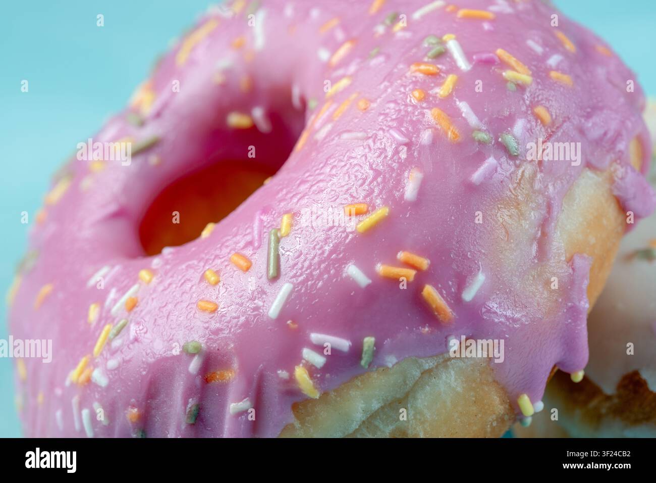 Extrem Nahaufnahme, die die glänzende Textur von rosa Fruchtglasur und mehrfarbigen Süßspritzeln auf einem frischen Gebäck zeigt Stockfoto