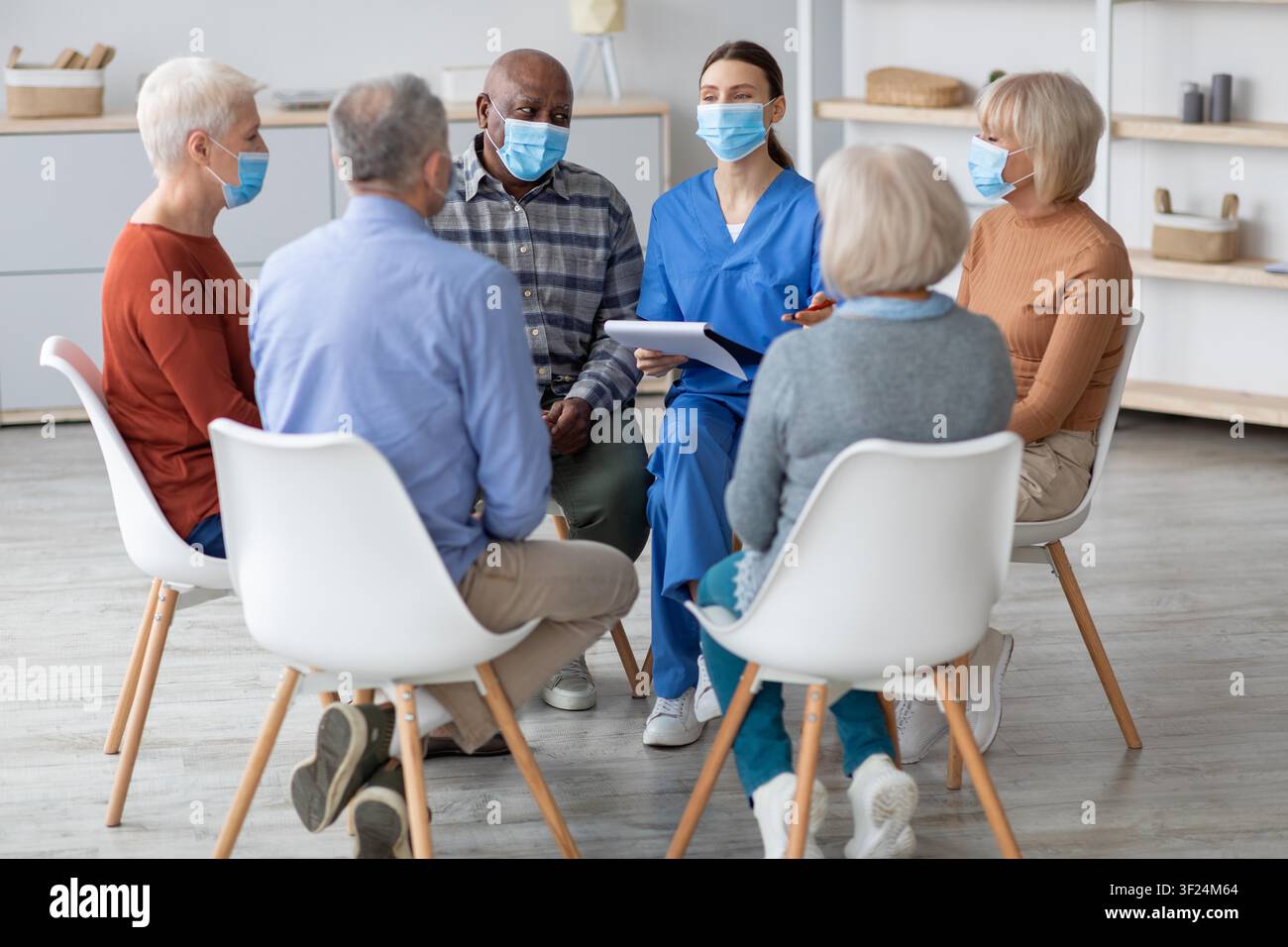 Gruppe von älteren Menschen, die in einem Unterstützungszirkel mit einem Gesundheitsfachkraft sprechen, Klinikumgebung Stockfoto