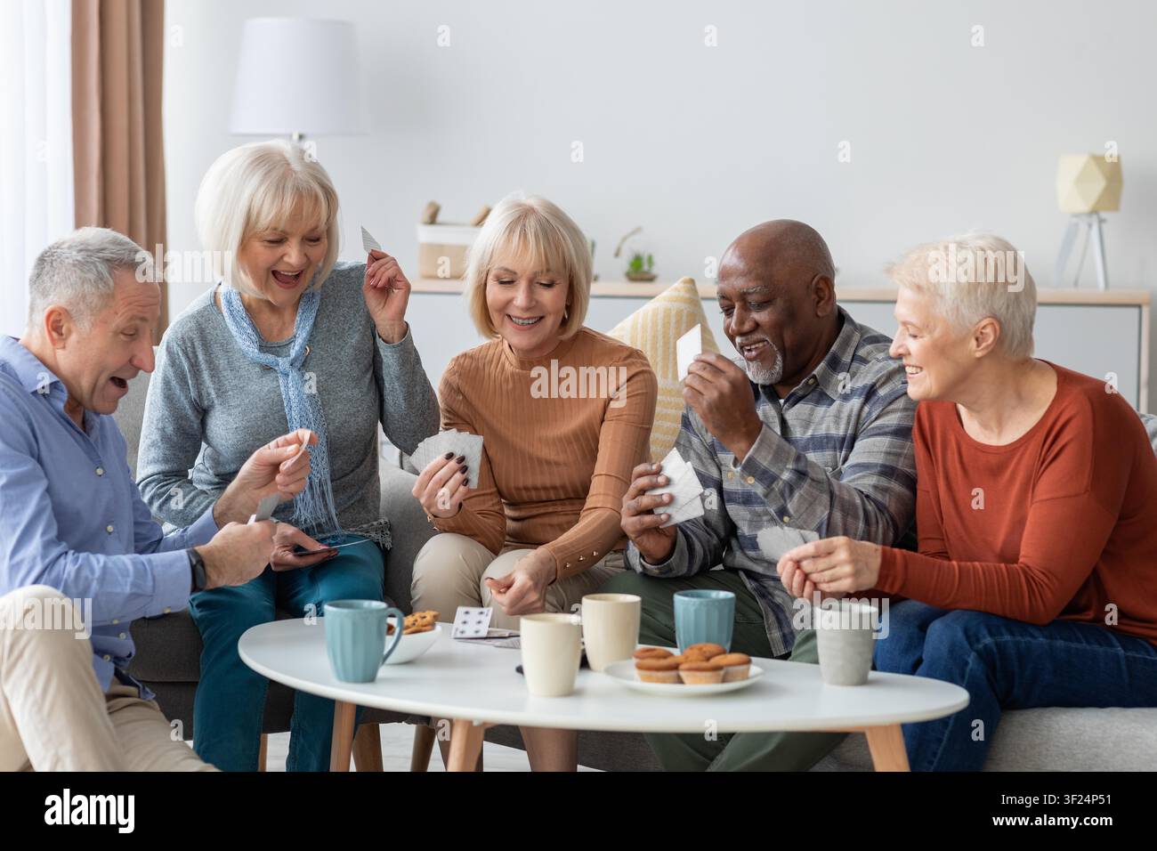 Glückliche Seniorengruppe spielt zusammen zu Hause Karten, lächelt und genießt das Leben Stockfoto