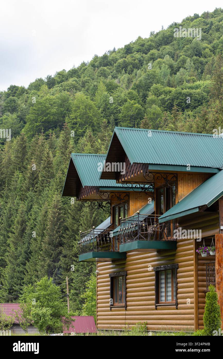 Ein mehrstöckiges Holzblockhaus mit Eisenbalkonen steht an einem steilen Hang, der mit dichtem Nadel- und Laubwald bedeckt ist. Stockfoto