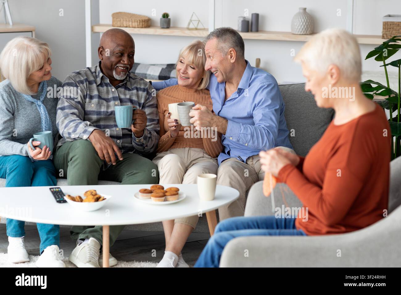 Glückliche diverse Gruppe von Seniorenfreunden, die Kaffee und Kekse zu Hause genießen, Lebensstilkonzept Stockfoto