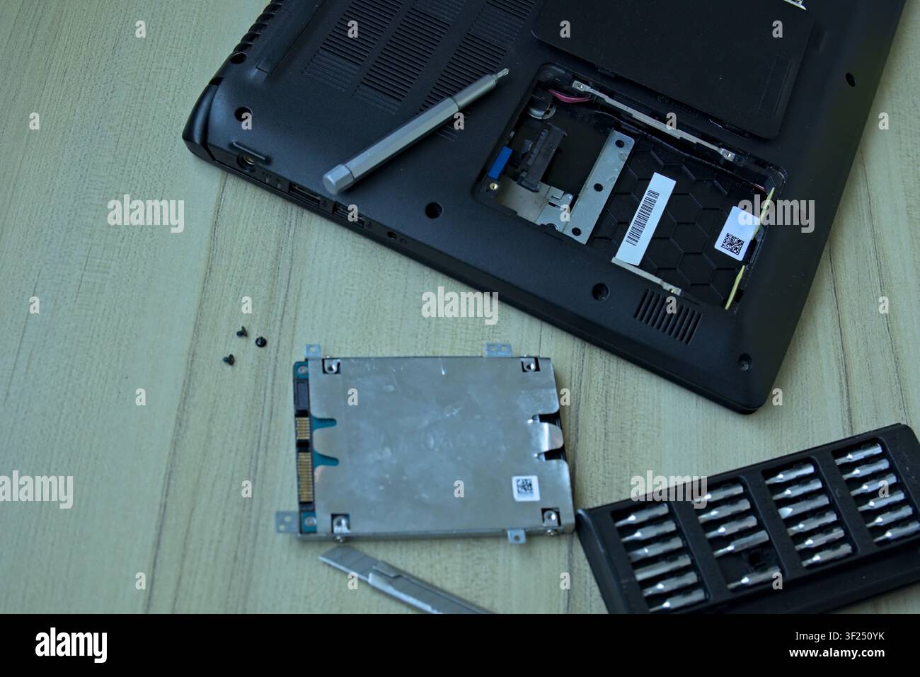 Hochwinkel-Flachlage eines offenen Laptops, der während eines Hardware-Upgrades auf einem Holztisch liegt. Neben dem Laptop befindet sich der entfernte 2,5-Zoll-Festplatten-Caddy, Stockfoto