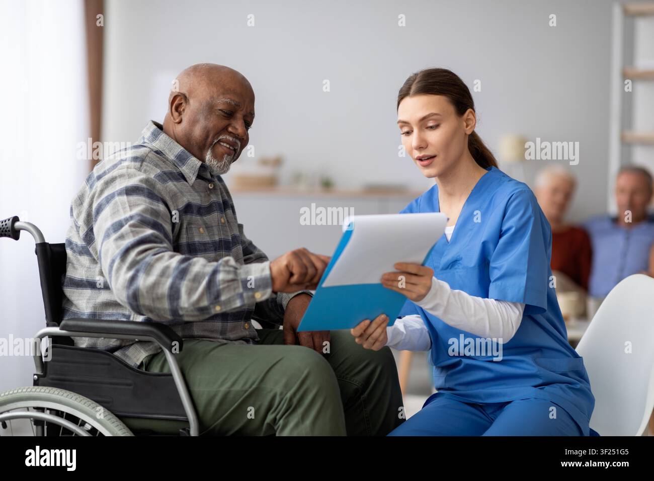 Lächelnder älterer afroamerikanischer Mann im Rollstuhl, der mit einer Krankenschwester in der Klinik spricht, Gesundheitskonzept Stockfoto