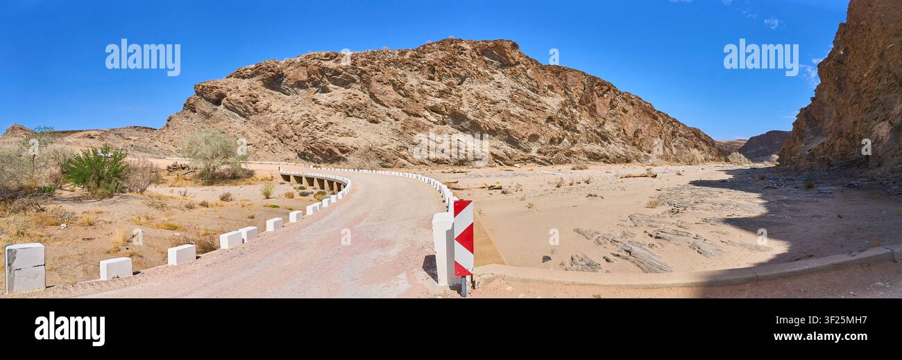 Eine Schotterstraße überquert eine niedrige Brücke durch die zerklüfteten Felsformationen des Gaub-Passes in der trockenen Wüstenlandschaft Namibias. Stockfoto