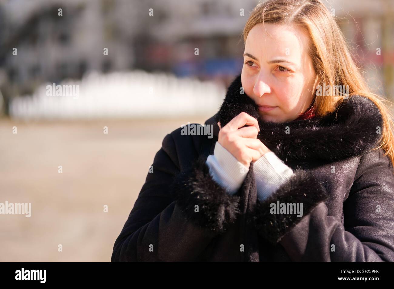 Traurige Frau, die weg schaut und sich warm hält, indem sie den Kragen ihres pelzgefütterten Mantels hochzieht Stockfoto