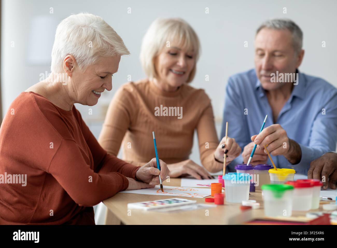 Zufriedene ältere kaukasische Frauen malen gemeinsam am Tisch, Konzept für Innenaktivität Stockfoto