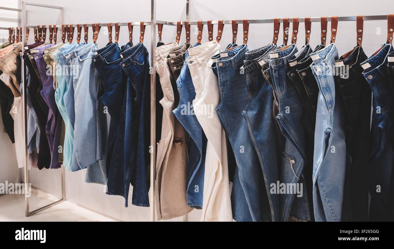 Kleiderständer hält mehrere Denimjeans. Hellblaue, dunkelblaue und beigefarbene Nuancen sind sichtbar. Jeans hängen ordentlich auf Bügeln in einem Einzelhandelsraum. Organisiert Stockfoto