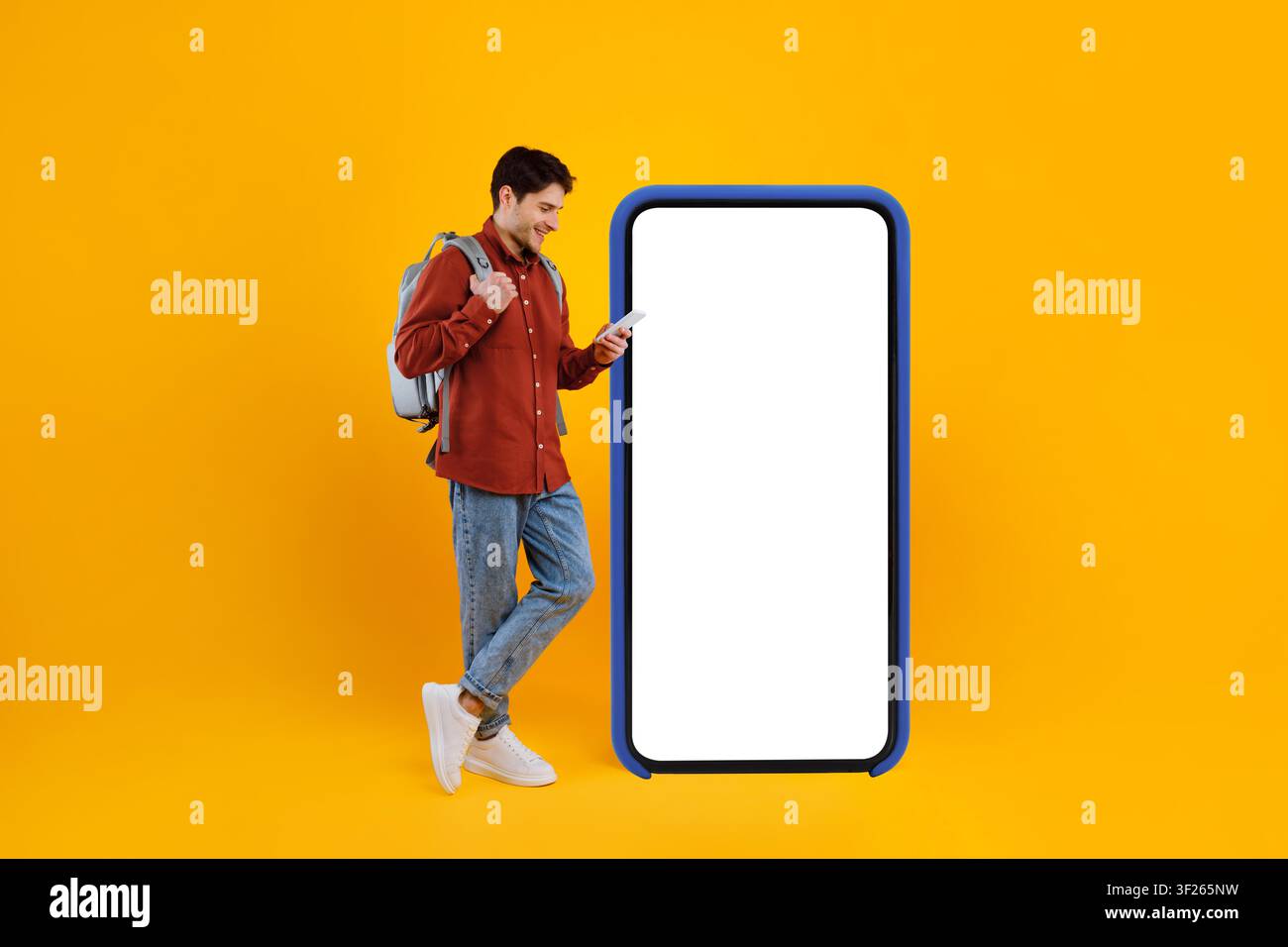 Lächelnder junger kaukasischer Mann, der ein Smartphone neben einer leeren Werbetafel benutzt, urbanes Konzept Stockfoto
