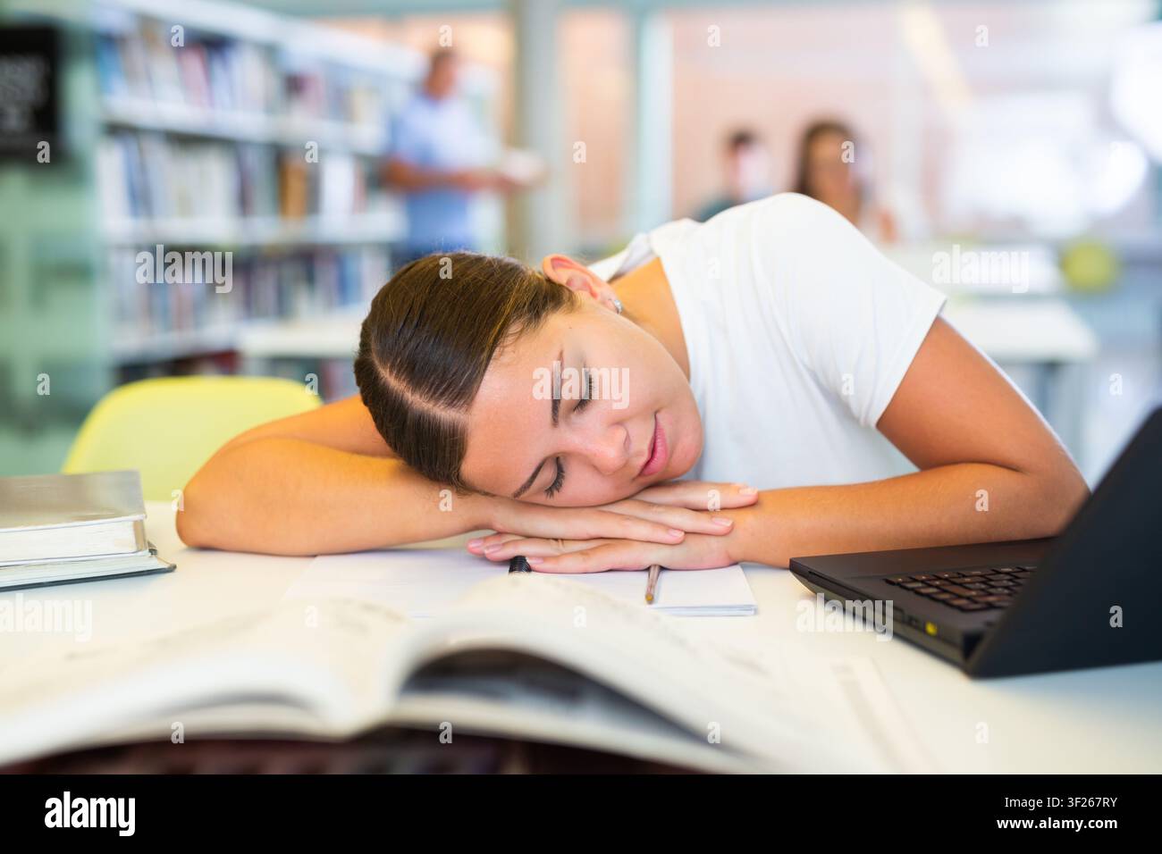 Müde Studentin schlief am Tisch in der Bibliothek ein Stockfoto