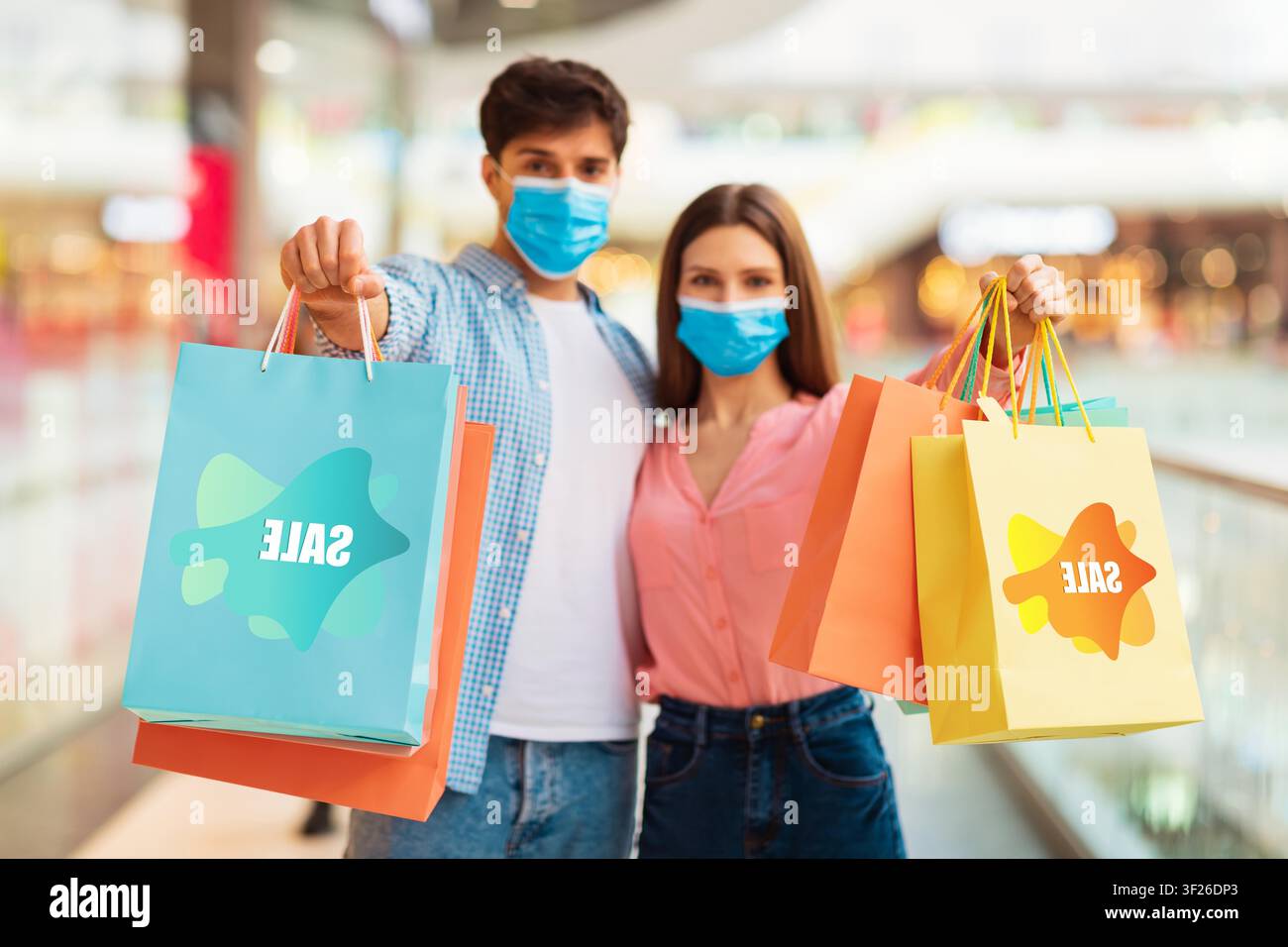 Junges Paar lächelt mit Einkaufstüten in der Mall, trägt Schutzmasken, Verkaufsbegriff Stockfoto