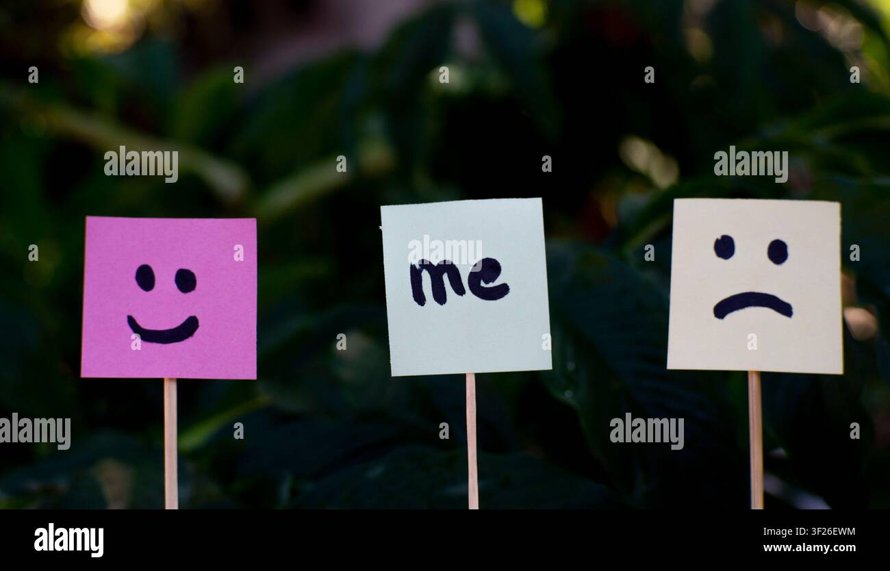 Notiz mit der Aufschrift „ich“ zwischen glücklichen und traurigen Emotionsgesichtern auf dunklem natürlichem Hintergrund, geeignet für Selbstidentität, sozialer Druck, Stimmung Stockfoto