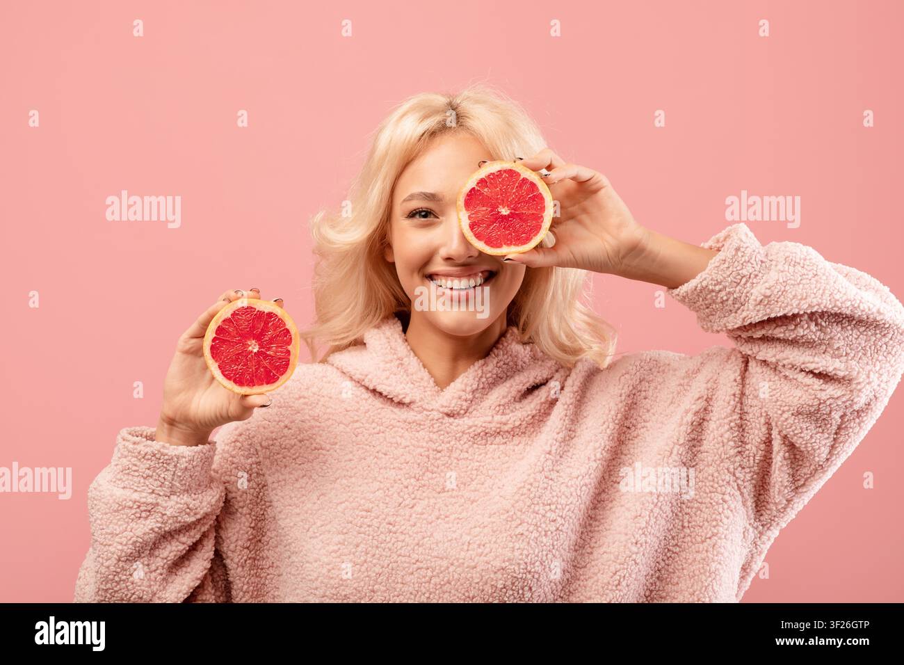 Glückliche junge Frau hält Grapefruitscheiben, lächelt in einem kuscheligen Pullover, Studio, Wellness-Konzept Stockfoto