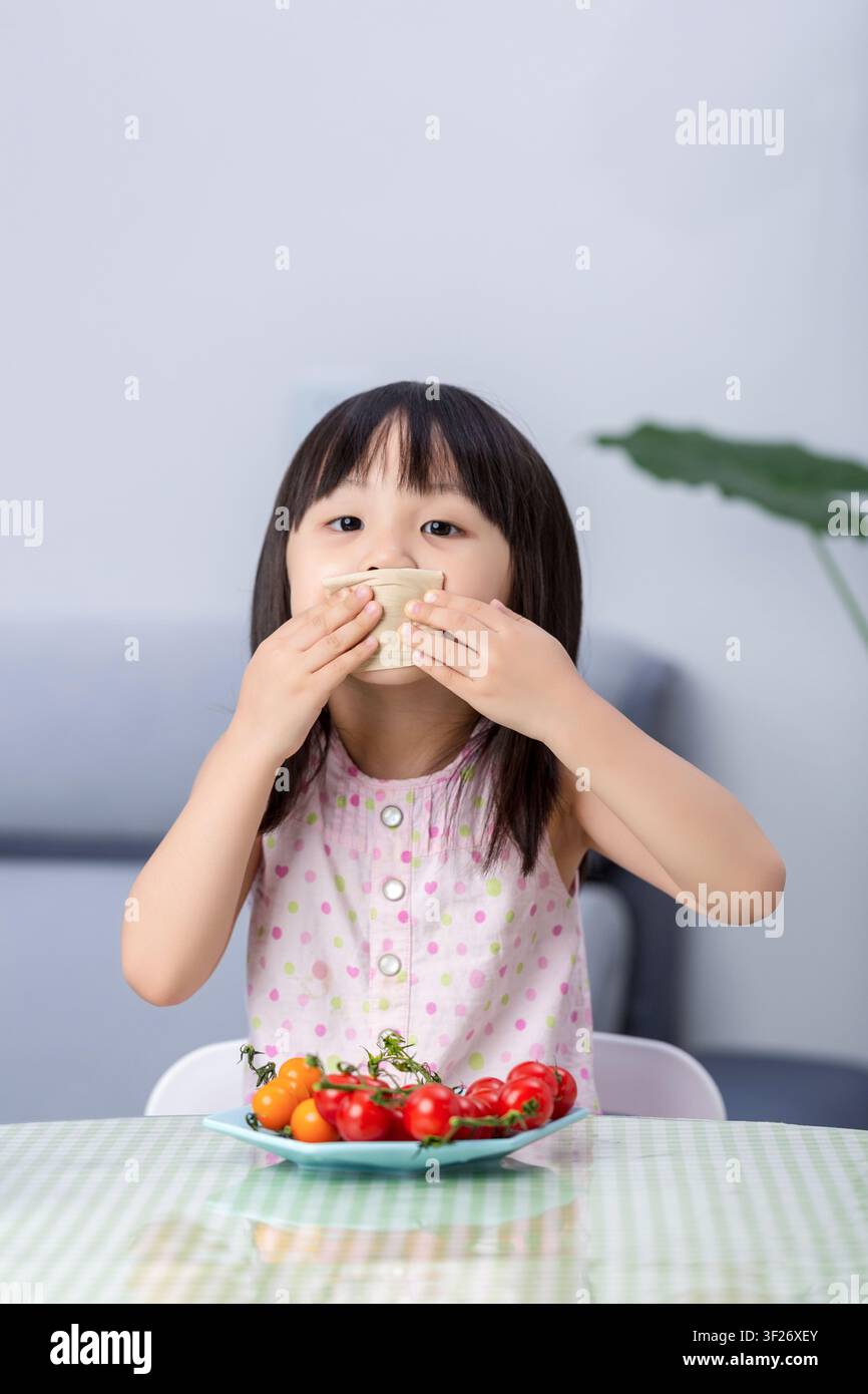 Ein asiatisches Mädchen wischt sich mit einer Serviette am Tisch den Mund ab und fördert gesunde Essgewohnheiten und Ernährungs Konzepte für Kinder. Stockfoto