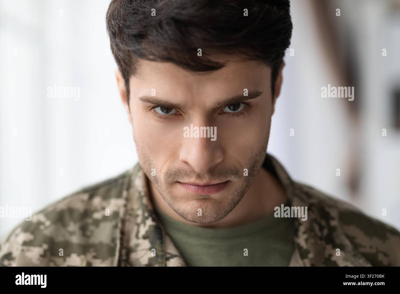 Männlicher Soldat mit konzentriertem Ausdruck in Tarnuniform, Inneneinstellung, ernstes Konzept Stockfoto