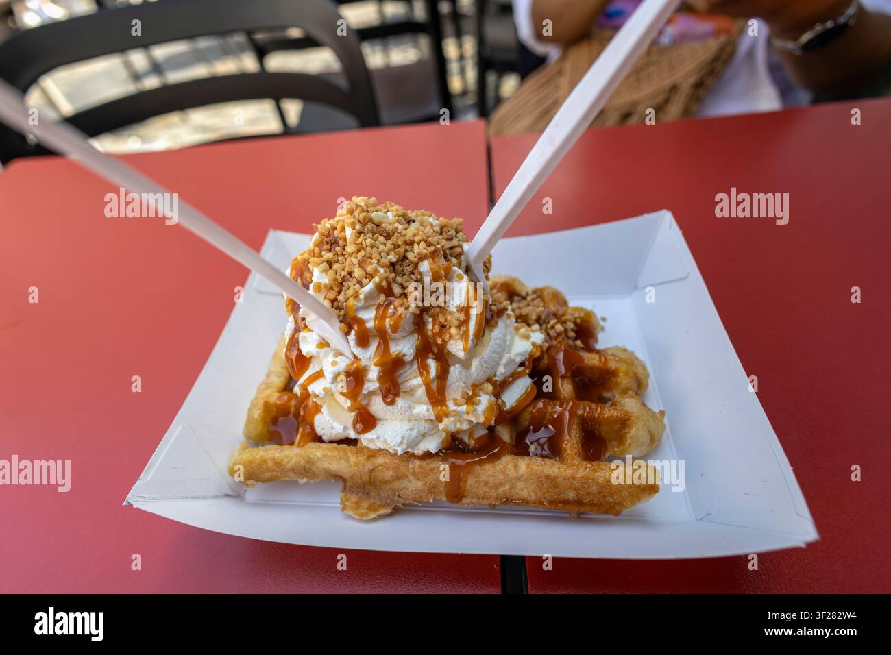 Liege-Waffel mit Schlagsahne-Topping, garniert mit Karamellsoße und einer Prise gehackter Haselnüsse oder zerbröckelten Speculoos-Keksen Stockfoto