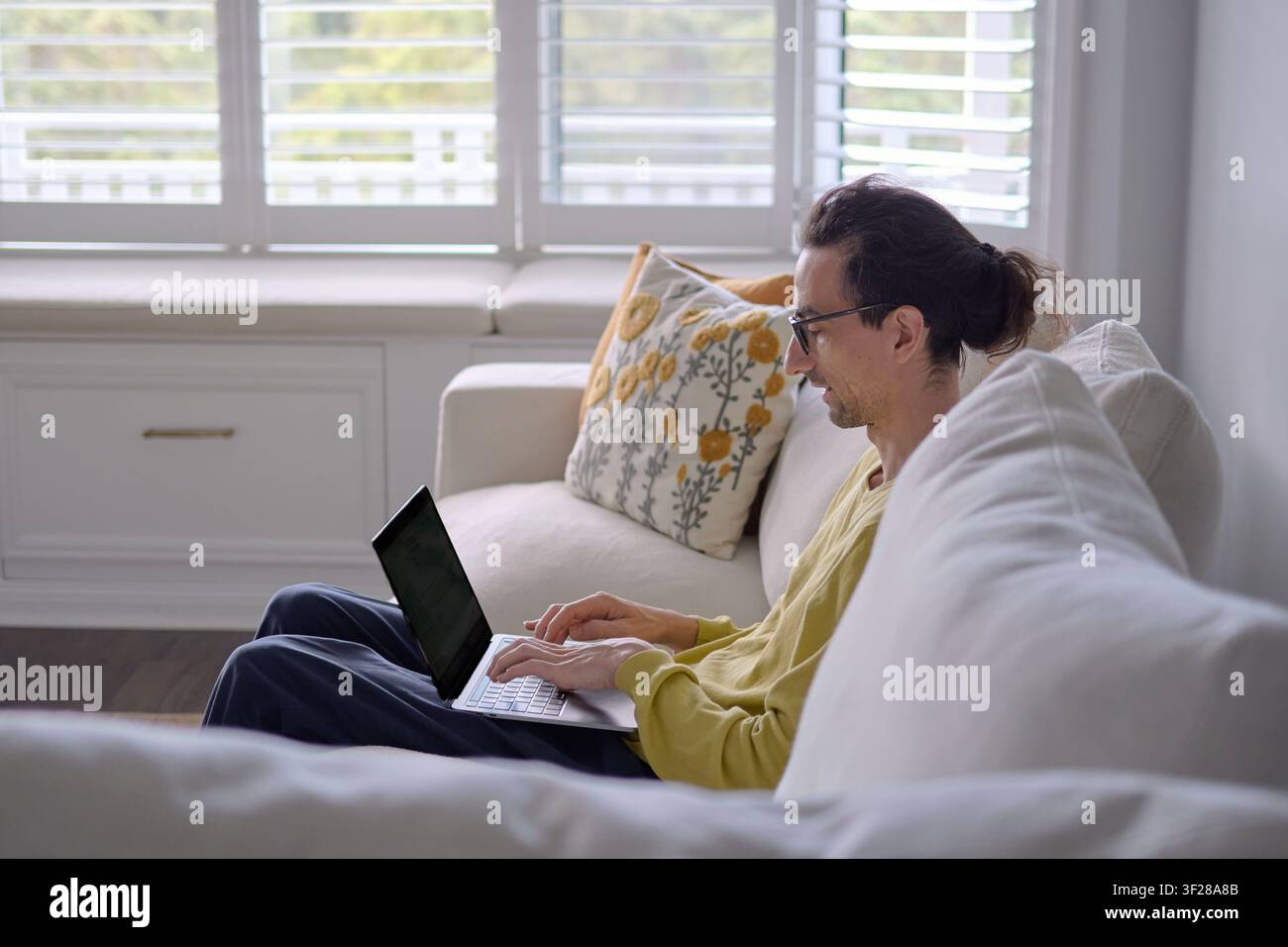 Mann tippt auf einem Laptop, während er auf der Couch im Wohnzimmer sitzt Stockfoto