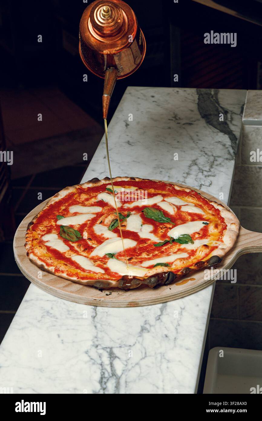 Ein Pizzaiolo sprüht Öl über eine frisch gebackene Margherita-Pizza. Stockfoto