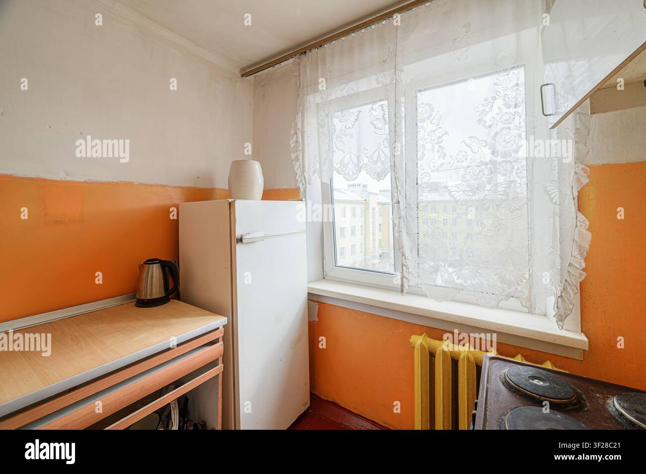 Kleine Küche. Kühlschrank, Fenster mit Spitzenvorhang, orangefarbene Wand und elektrischer Wasserkocher. Vintage-Innerelemente Stockfoto