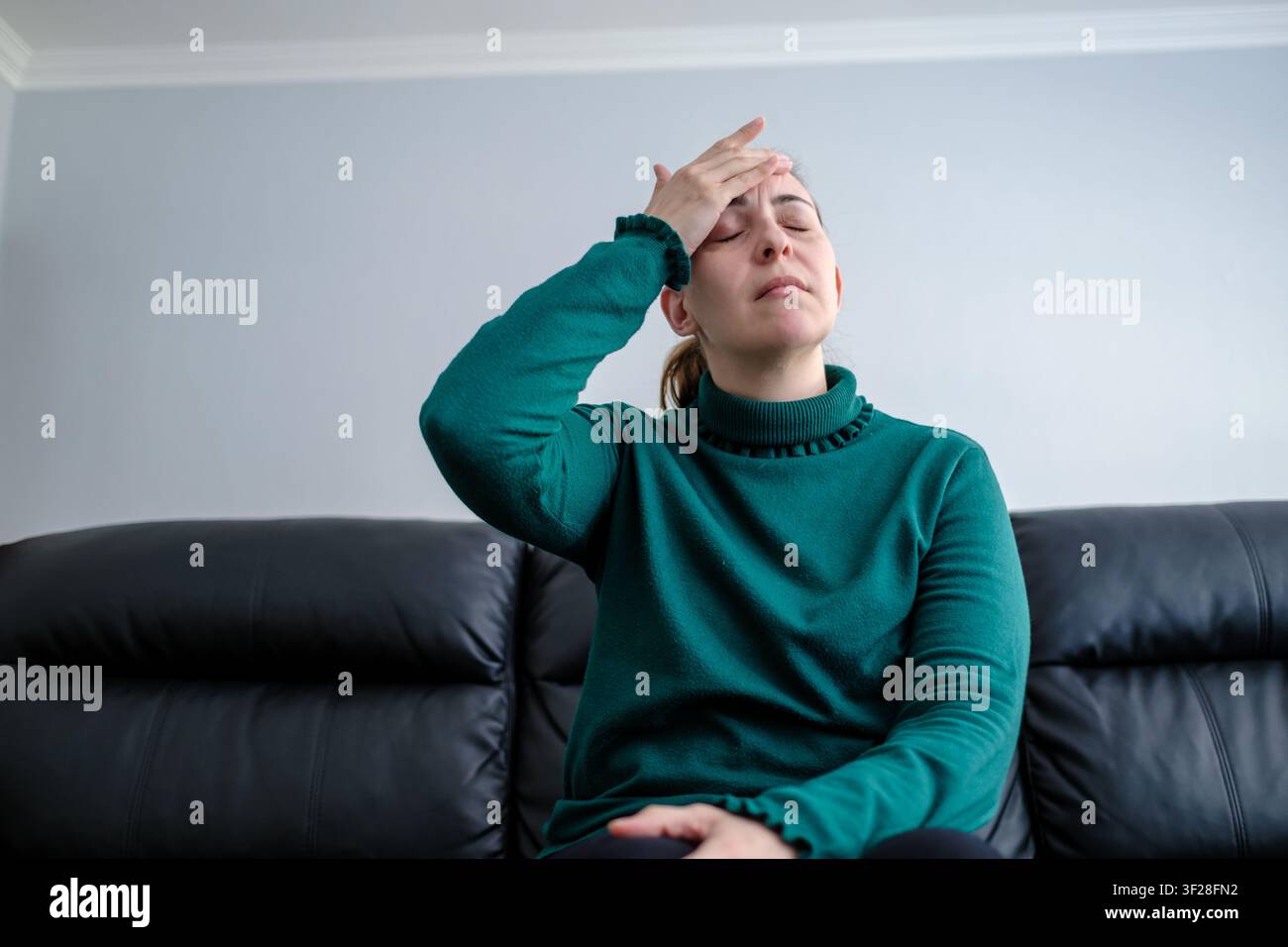 Frau, die Schmerzen durch Kopfschmerzen oder Migräne verspürt, sitzt auf dem Sofa zu Hause Stockfoto
