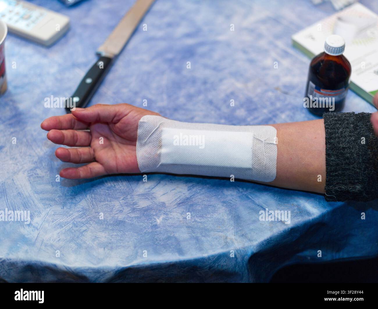 ein selbstverletzteter Arm mit einem Pflaster und Erste Hilfe auf dem Tisch, Innenraum-Nahaufnahme Stockfoto