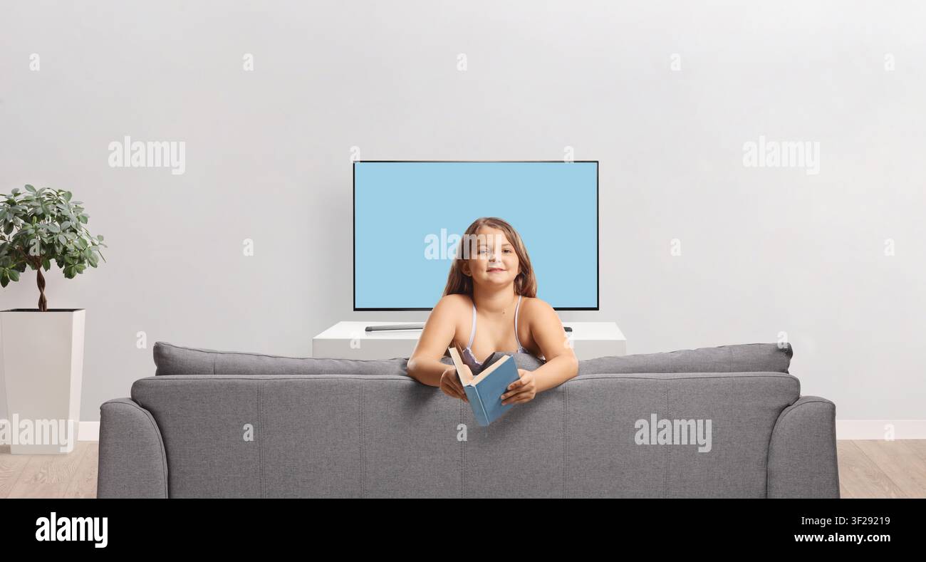 Mädchen auf einem Sofa, das ein offenes Buch hält, isoliert auf weißem Hintergrund Stockfoto