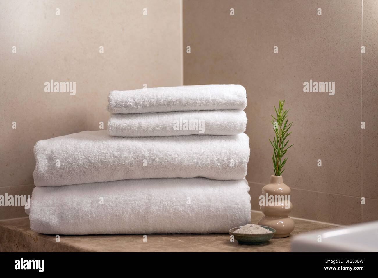 Gerolltes weißes Handtuch auf einem hölzernen Badetablett mit Spa-Zubehör in einem modernen Hotelbadezimmer, das eine entspannende Wellness-Atmosphäre schafft Stockfoto