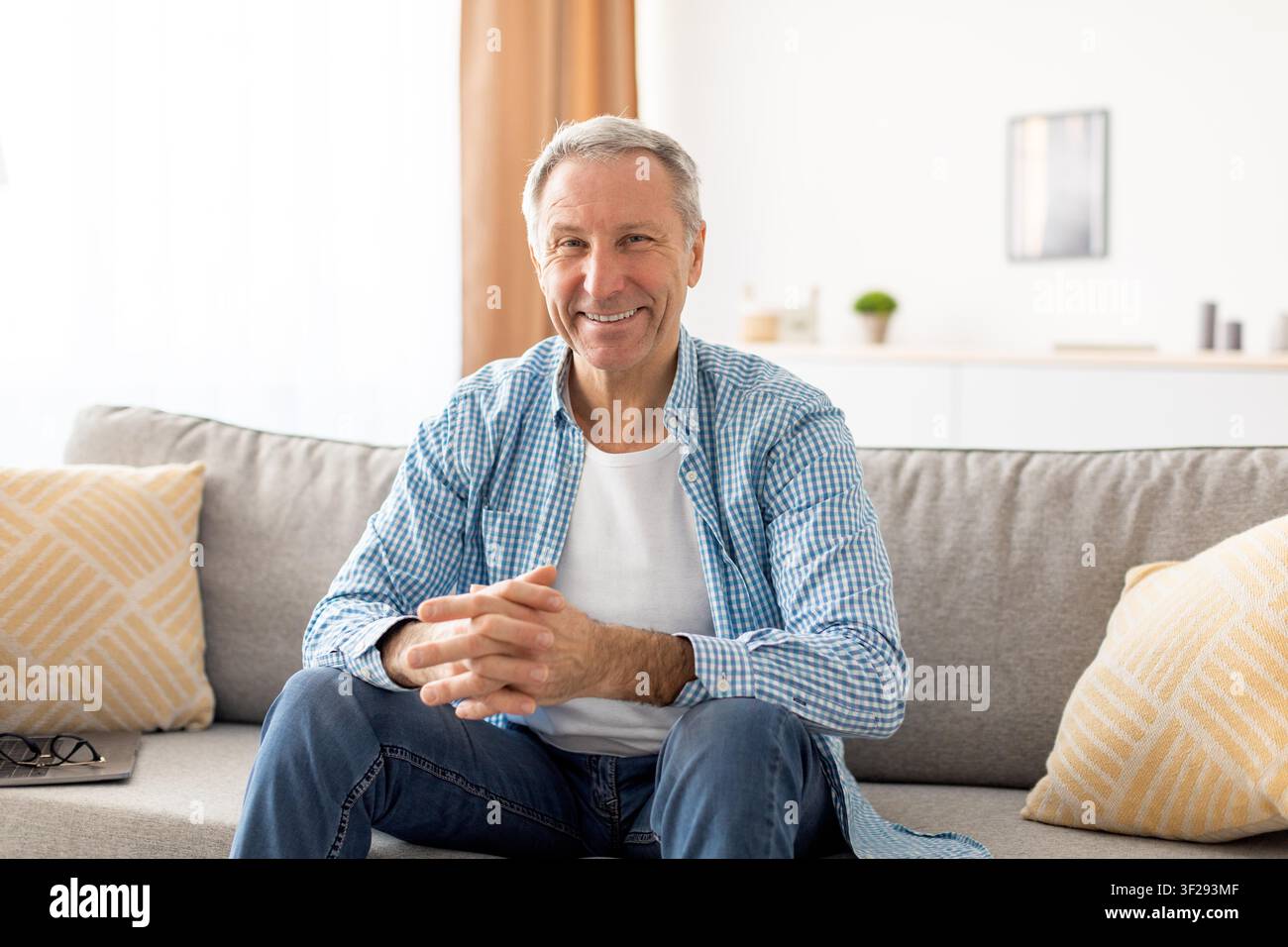 Lächelnder älterer kaukasischer Mann sitzt auf dem Sofa, entspannte Heimatmosphäre Stockfoto