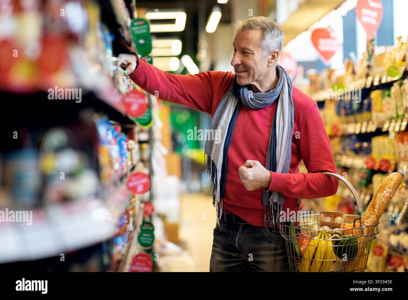 Zufriedener älterer kaukasischer Mann beim Einkaufen im Supermarkt, der frische Produkte auswählt Stockfoto