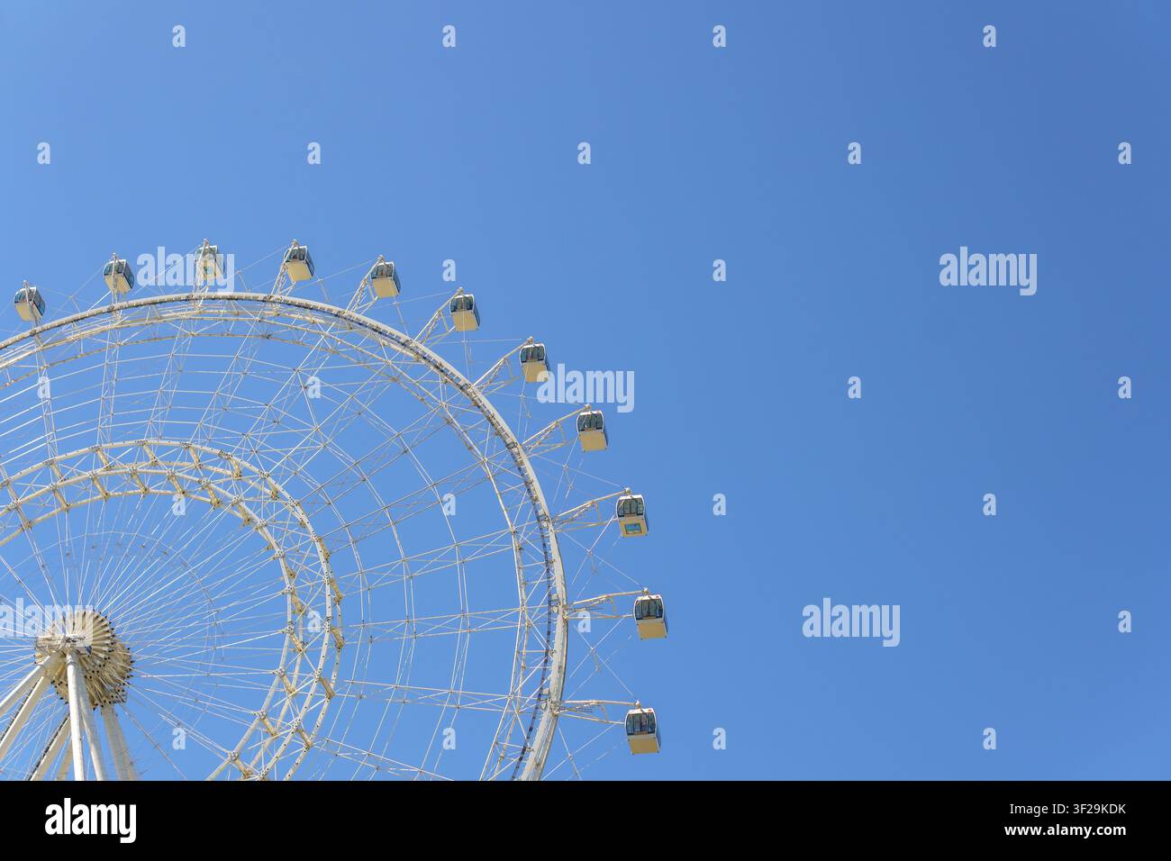 Riesenrad auf der linken Seite mit einem weiten klaren blauen Himmel auf der rechten Seite. Große Vergnügungsanlage mit Passagierkabinen unter hellem Sonnenlicht. Stockfoto