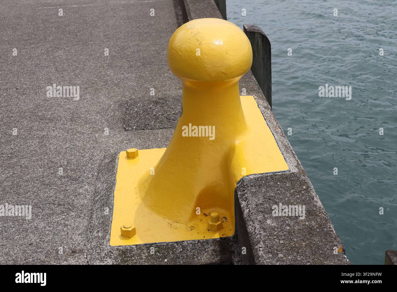 gelber maritimer Ankerpfosten, Gusseisen oder Stahlguss, direkt in Betonkai verankert (Nahaufnahme, Ufer) Stockfoto