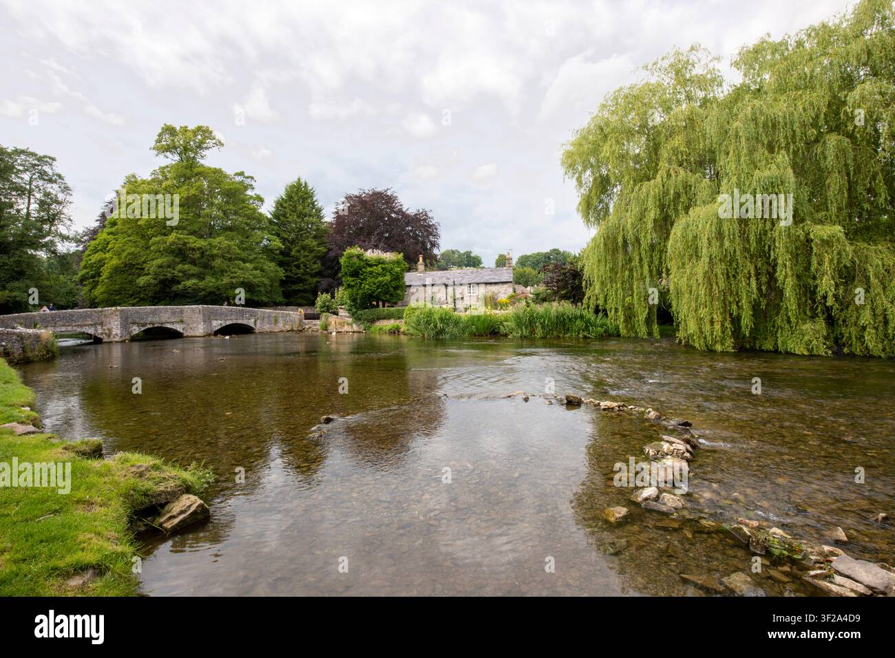 Die historische Stein-Sheepwash-Brücke und ein traditionelles Cottage neben den klaren Gewässern des Flusses Wye in Ashford in the Water, Derbyshire, UK. Stockfoto