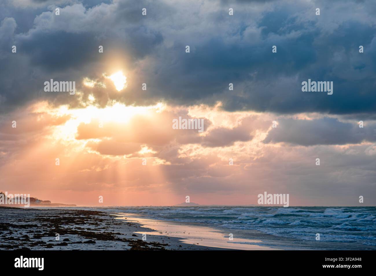 Wunderschöner Sonnenuntergang über dem Strand mit dramatischen Wolken und schimmernden Meereswellen. Stockfoto