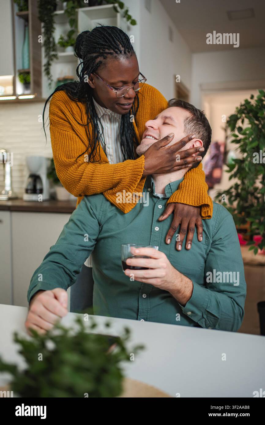 Liebevolles interrassisches Paar, das sich in moderner Küche zu Hause umschließt Stockfoto