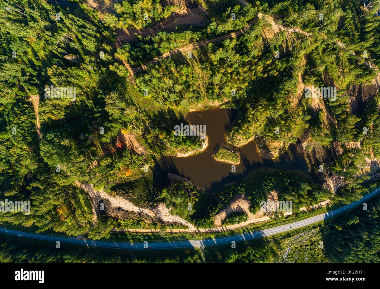 Luftbild eines kleinen Teiches, umgeben von dichtem Wald, Schotterwegen und einer Straße in Lettland. Stockfoto
