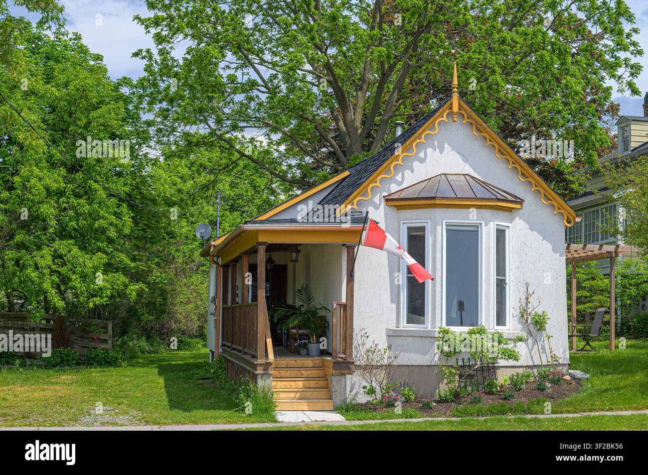 Charmantes Haus im Cottage-Stil mit dekorativer Zierleiste, überdachter Veranda und kanadischer Flagge Stockfoto